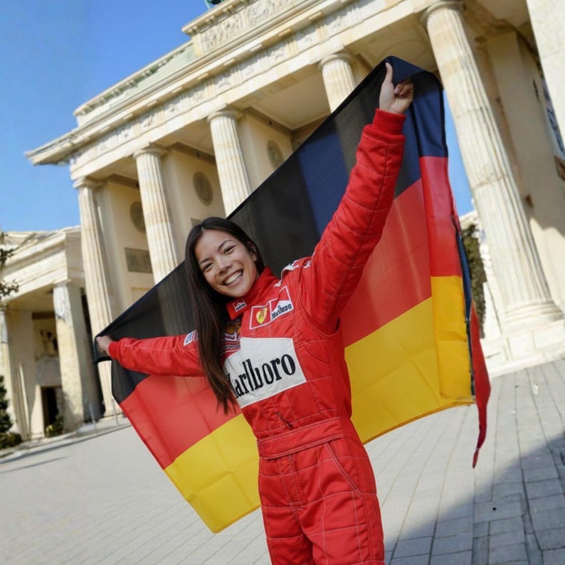 May include: A person in a red racing suit holds a German flag in front of the Brandenburg Gate. The flag is black, red, and yellow. The racing suit has the Marlboro logo.