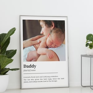 Puede incluir: Impresión enmarcada con una fotografía de un bebé descansando sobre el hombro de una persona. La palabra "Daddy" y su definición están impresas debajo. El marco es plateado.