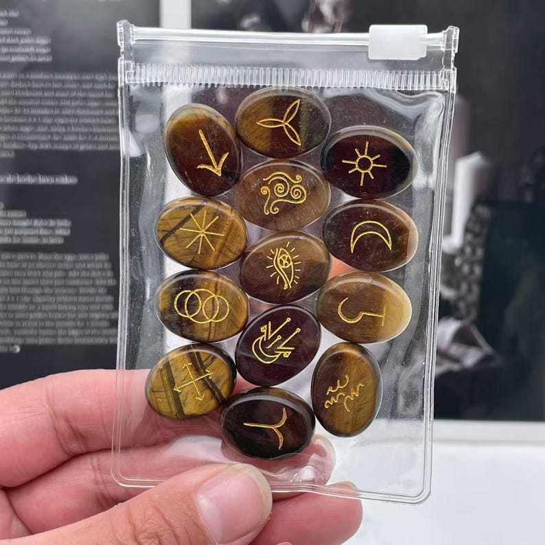 May include: A clear plastic bag filled with 13 oval-shaped tiger's eye stones. Each stone has a different gold symbol etched on the surface.