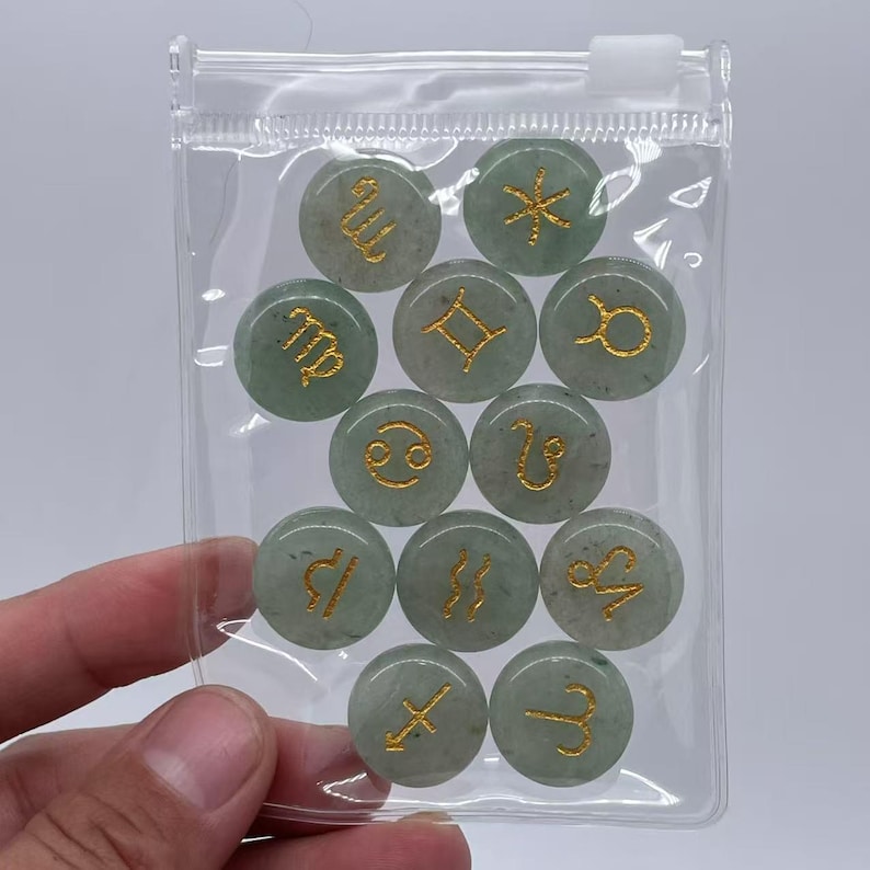 May include: A clear plastic bag containing 12 green gemstone zodiac signs with gold lettering. The signs include Aries, Taurus, Gemini, Cancer, Leo, Virgo, Libra, Scorpio, Sagittarius, Capricorn, Aquarius, and Pisces.