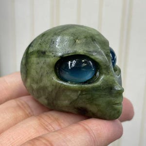 Peut inclure: Une sculpture de tête d'extraterrestre en pierre verte avec de grands yeux bleus. La sculpture est sculptée à la main et a une finition lisse et polie. La tête d'extraterrestre est un objet décoratif unique.