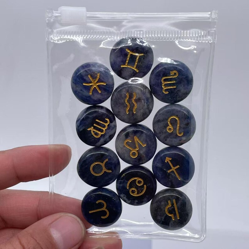 May include: A clear plastic bag filled with twelve blue and white gemstone zodiac signs. Each sign has a gold zodiac symbol on it.