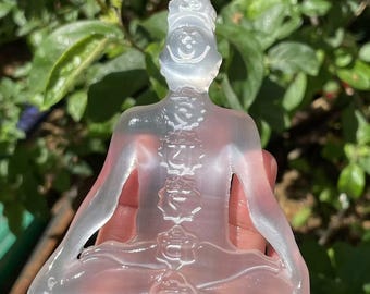 Könnte beinhalten: Eine transparente Glasskulptur einer Person, die in meditativer Haltung sitzt, mit detaillierter Wirbelsäule und Chakren. Die Skulptur ist durchscheinend und hat einen leichten irisierenden Schimmer.