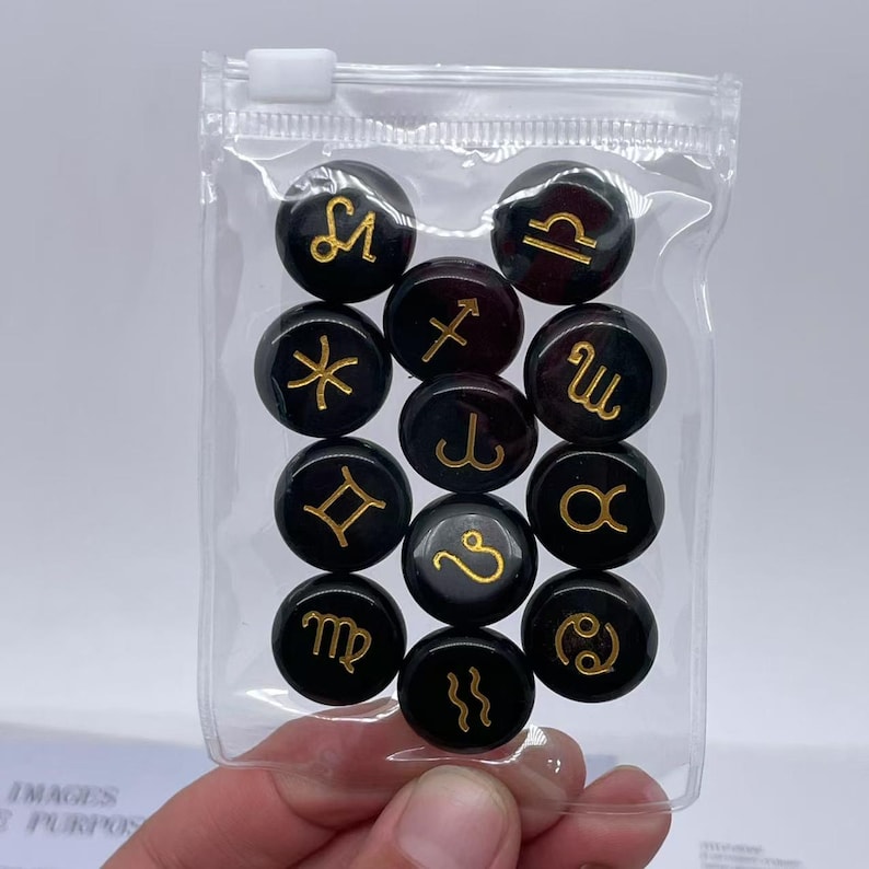 May include: A clear plastic bag filled with twelve black round tokens. Each token has a gold zodiac symbol on it.
