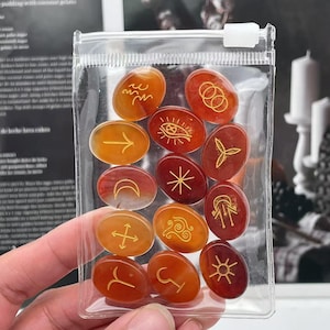 May include: A set of 12 oval-shaped carnelian stones with gold-colored symbols. The stones are in a clear plastic bag.