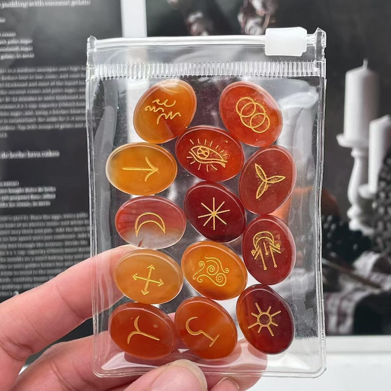 May include: A set of 12 oval-shaped carnelian stones with gold-colored symbols. The stones are in a clear plastic bag.