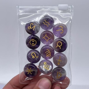 May include: A clear plastic bag filled with twelve round amethyst stones, each with a gold zodiac symbol. The symbols are: Aquarius, Aries, Cancer, Capricorn, Gemini, Leo, Libra, Pisces, Sagittarius, Scorpio, Taurus, and Virgo.