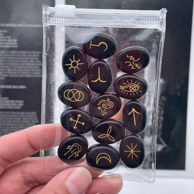 May include: A set of 12 black oval-shaped stones with gold symbols. The stones are in a clear plastic bag.