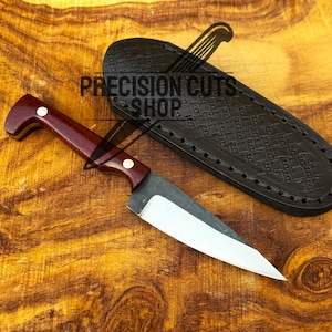 May include: A handcrafted knife with a dark wood handle and a silver blade, next to a black leather sheath. The knife has a full tang construction. The text "PRECISION CUTS SHOP" is visible on the image.