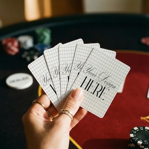 May include: A hand holding a fan of playing cards with a grid pattern and the text "Your Design HERE". The cards are on a red and black poker table with poker chips in the background.