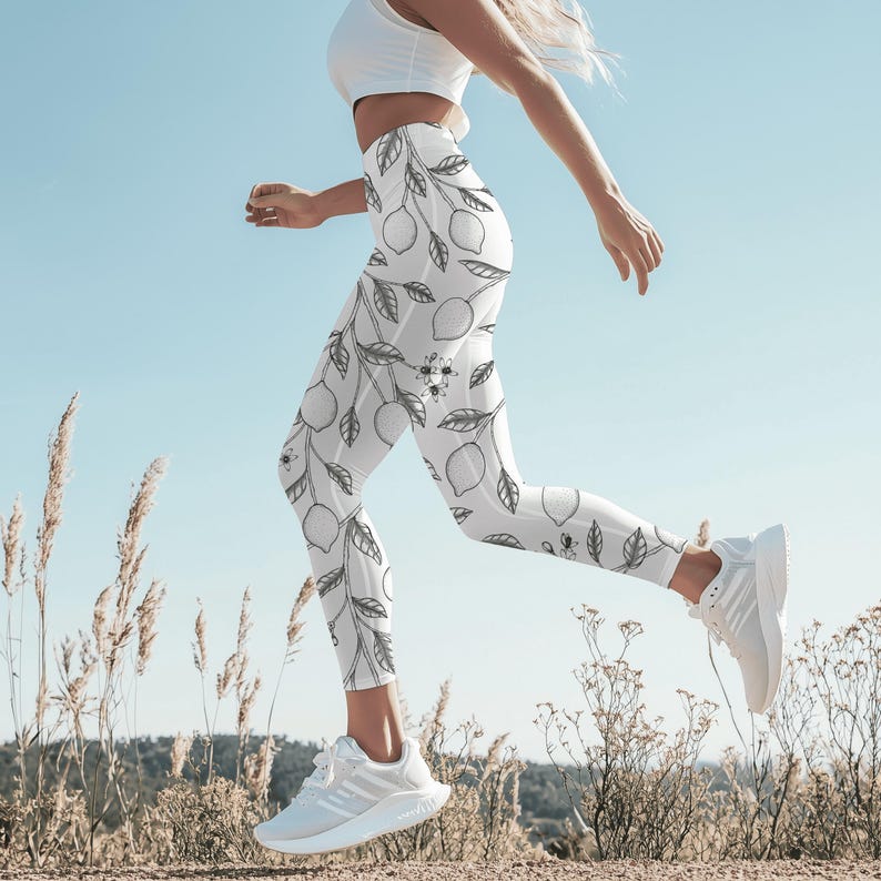 May include: White leggings with a black lemon and leaf pattern. The leggings are worn with a white top and white athletic shoes. The person is running outside on a sunny day.