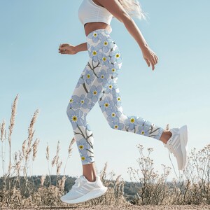 May include: White leggings with a light blue floral pattern featuring yellow centers. The leggings are worn with a white top and white athletic shoes. The person is running outdoors on a sunny day.