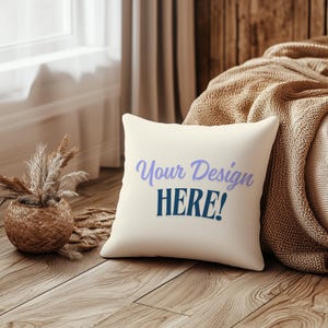 May include: A white throw pillow with the text "Your Design HERE!" in blue and purple lettering. The pillow is sitting on a wooden floor next to a woven basket with dried grass.