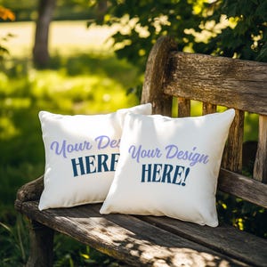 May include: Two white throw pillows with the text "Your Design HERE!" printed in purple and blue on a wooden bench. The pillows are sitting on a wooden bench in a garden setting.