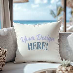 May include: A white cushion with the text "Your Design HERE!" in purple and blue lettering. The cushion is on a light grey sofa with a wicker basket and a pineapple on the table.