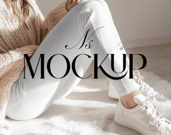 May include: A mockup image featuring a person wearing a beige knit sweater, white ribbed leggings, and white sneakers. The person is seated on a white fluffy rug. The text "Ns MOCKUP" is overlaid on the image.