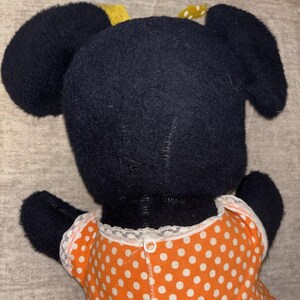 May include: A handmade plush toy featuring a black head with large, rounded ears and a yellow bow. The toy is wearing an orange dress with white polka dots and white lace trim.