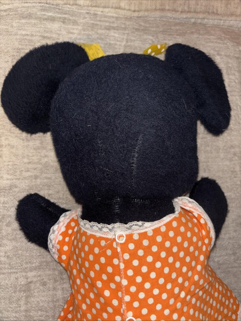 May include: A handmade plush toy featuring a black head with large, rounded ears and a yellow bow. The toy is wearing an orange dress with white polka dots and white lace trim.