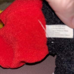 May include: A plush toy featuring a bright red fabric section adjacent to a textured black fabric area. A white rectangular fabric tag is attached to the side, displaying printed text that includes the words SURFACE WASHABLE ONLY.