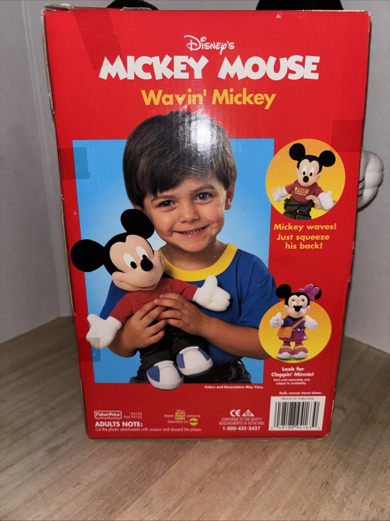 May include: A red box featuring Disney's Mickey Mouse Wavin' Mickey toy. The box has images of Mickey Mouse and a child holding the toy. Text on the box includes "Mickey waves! Just squeeze his back!" and "Look for Cloppin' Minnie!"