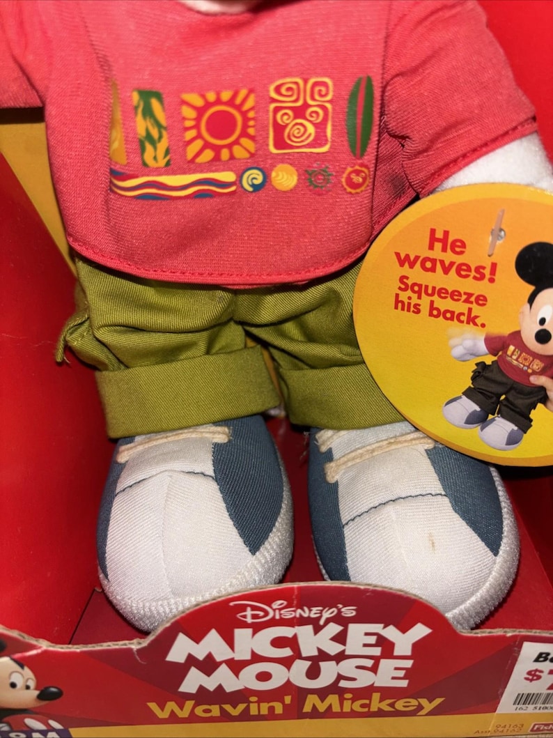 May include: A Mickey Mouse plush doll wearing a red shirt with colorful graphics, green pants, and blue and white sneakers. The doll is in a red box with the text "Disney's Mickey Mouse Wavin' Mickey". A tag says "He waves! Squeeze his back."