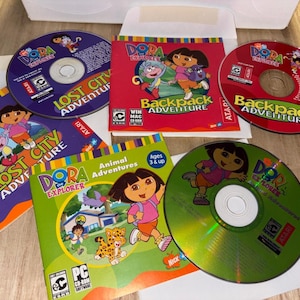 Puede incluir: Una colección de juegos de CD-ROM de Dora la Exploradora para PC y Mac. Las portadas son rojas, moradas y verdes, con Dora y otros personajes. Los títulos incluyen "Lost City Adventure", "Backpack Adventure" y "Animal Adventures".