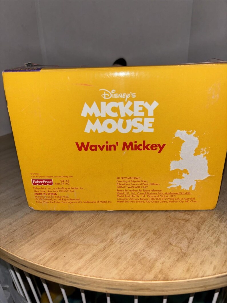 May include: A yellow box featuring the Disney's Mickey Mouse logo and the text "Wavin' Mickey" in white and red. The box includes text about the product's materials and manufacturer, Fisher-Price.