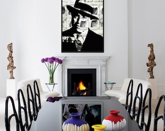 May include: A black and white framed artwork of a person wearing a hat and suit hangs above a fireplace. A black dining table is in the foreground, with colorful vases. The room has white walls, chairs, and sculptures.