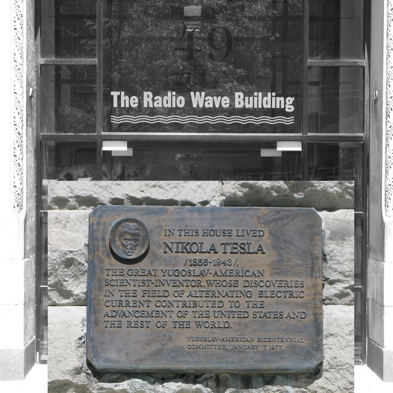 May include: A black and white photo of a plaque commemorating Nikola Tesla, a Serbian-American inventor, scientist, and engineer. The plaque is mounted on a stone wall and reads "In this house lived Nikola Tesla / 1856-1943/, The Great Yugoslav-American Scientist-Inventor, whose discoveries in the field of alternating electric current contributed to the advancement of the United States and the rest of the world. Yugoslav-American Bicentennial Committee, January 7, 1977."