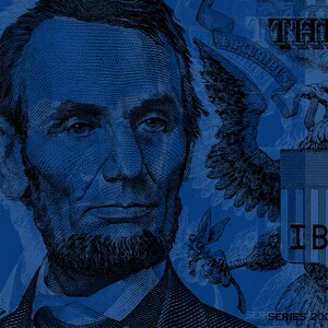 May include: A close-up of a blue and white US dollar bill featuring a portrait of Abraham Lincoln. The bill also features the words "The United States of America" and "One Dollar" in blue lettering. The bill is in focus, while the background is blurred.