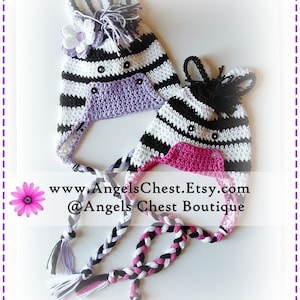 May include: Two crocheted zebra hats with black and white stripes, one with a purple flower and the other with a pink flower. The hats have black eyes and a black nose. The hats are tied together with a braided cord.