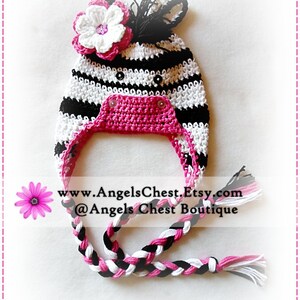 May include: A black and white striped crocheted hat with a pink flower and a pink crocheted chin strap. The hat has a black and white braided tail. www.AngelsChest.Etsy.com @Angels Chest Boutique