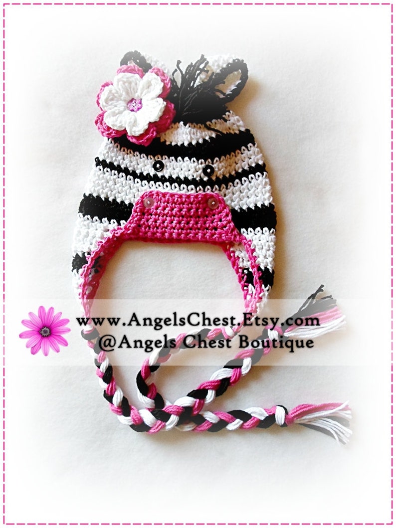 May include: A black and white striped crocheted hat with a pink flower and a pink crocheted chin strap. The hat has a black and white braided tail. www.AngelsChest.Etsy.com @Angels Chest Boutique