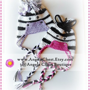 Puede incluir: Dos gorros de cebra tejidos a crochet con rayas blancas y negras, uno con forro morado y el otro con forro rosa. Ambos gorros tienen orejas negras y una crin negra. Los gorros están atados juntos con largos cordones trenzados negros, blancos y rosas. El texto "www.AngelsChest.Etsy.com @Angels Chest Boutique" es visible en la imagen.