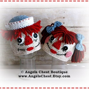 May include: Two crocheted doll hats, one with a blue and white sailor hat and the other with red yarn hair and blue bows. Both hats have a red nose, black eyes, and a stitched smile.