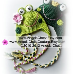 May include: Two green crocheted frog hats with pink and white accents. The hats have large, white eyes and a pink smile. The hats are connected by a long, braided cord with pink, white, and green strands. The text on the image reads: "www.AngelsChest.Etsy.com www.AngelsChestCouture.Etsy.com @2010-2012 Angels Chest"