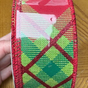 May include: Red and green plaid ribbon with a glittery finish. The ribbon is wrapped around a spool and has a red edge.