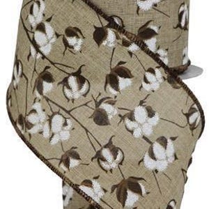 May include: A roll of decorative ribbon featuring a cotton plant design. The ribbon has a tan background with white and brown cotton blossoms and stems. The edges are trimmed with a dark brown stitch.