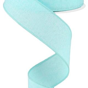 May include: A roll of light blue ribbon with a textured, linen-like appearance. The ribbon is unwound, creating a flowing, decorative element. The ribbon is approximately 2.5 inches wide.