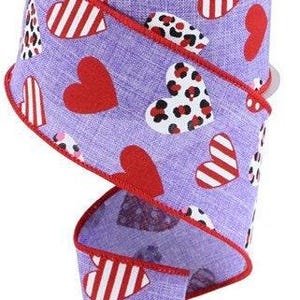 May include: A roll of decorative ribbon featuring a lavender background with red hearts, striped hearts, and leopard print hearts. The ribbon has a red trim and is perfect for crafts and gift wrapping.