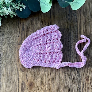 May include: A pink crocheted baby bonnet with a scalloped edge and a tie.