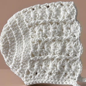 May include: White crocheted baby bonnet with a scalloped edge and ties.