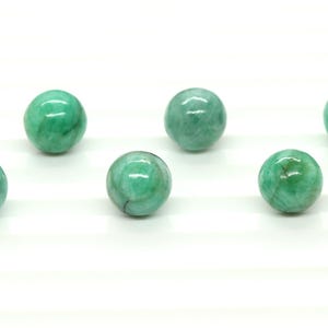 May include: Six polished, round, green gemstone spheres are displayed against a white backdrop. The spheres have a marbled effect with varying shades of green. These gemstones are likely used for decorative or metaphysical purposes.