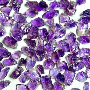 May include: A collection of raw amethyst crystals, showcasing a range of deep purple hues. The crystals are irregularly shaped, with a natural, unpolished appearance. The image is taken from a top-down perspective, highlighting the varying sizes and textures of the gemstones.