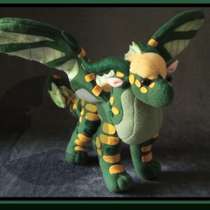 K&ouml;nnte beinhalten: Ein LeafWing-Drachenpl&uuml;schtier mit gr&uuml;nen, gelben und beigen Akzenten. Das Bild enth&auml;lt den Text "LeafWing Plush Pattern" und "English PDF Sewing Pattern & Instructions!". Das Muster ist f&uuml;r Fortgeschrittene und erfordert keine Stickerei.