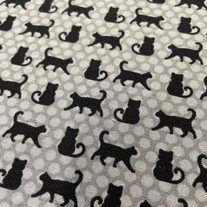 May include: A fabric featuring a repeating pattern of solid black cat silhouettes alternating between sitting and walking poses, set against a light gray background covered in a dense grid of small, white, circular polka dots.