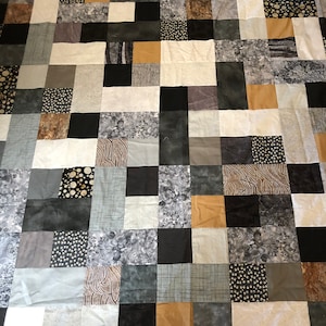 May include: A patchwork quilt made of various shades of gray, black, and brown fabric squares. The quilt has a geometric pattern and features different textures and patterns within each square.