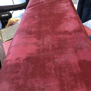 Może przedstawiać: Zbliżenie na głęboko czerwony materiał o fakturowanej, lekko marmurkowej powierzchni. Materiał jest złożony i wydaje się być materiałem do pikowania lub tapicerki.