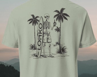 May include: A light green t-shirt with a black and white illustration of a skeleton holding a bottle and a surfboard with the word "LOHIKO" written on it. The skeleton is standing on a beach with palm trees.