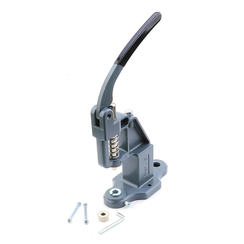 May include: A gray metal snap press machine with a black handle. The machine has a spring and is accompanied by several small metal parts, including screws and a wrench. The base has a circular opening.